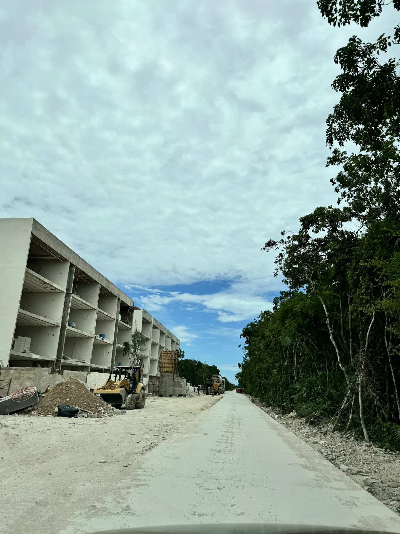 Access road being poured beside a development still in structure, with a mixer truck and a loader working