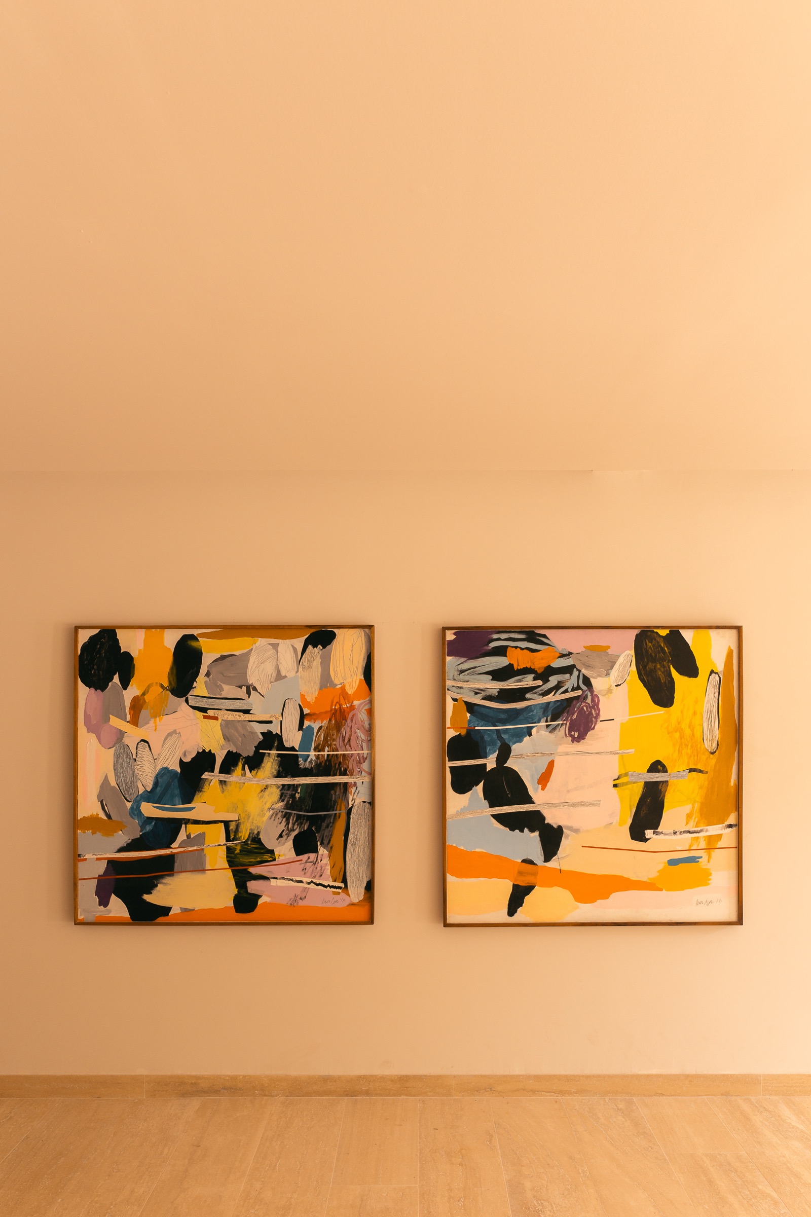 Photograph of two large square abstract canvases on an apricot wall above a pale plank floor