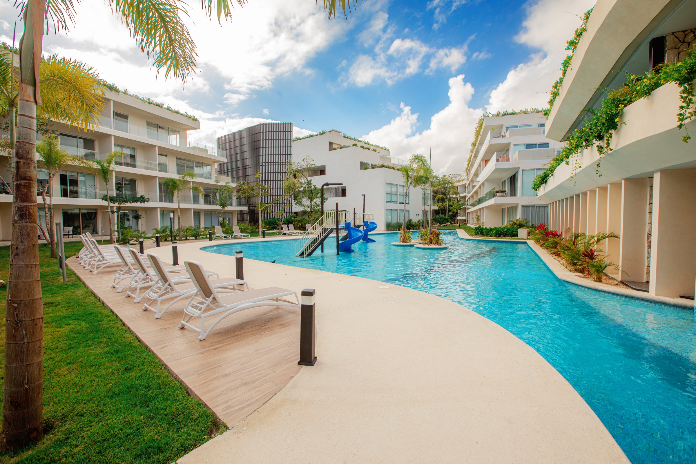 Central pool at The Leaf Condos Playacar with sun loungers, a water slide and the four-storey wings on both sides