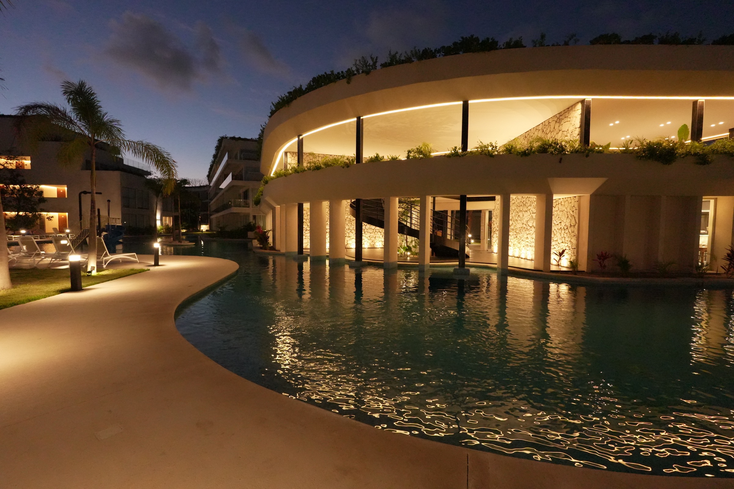 Clubhouse at The Leaf Condos Playacar lit at dusk with the pool in the foreground