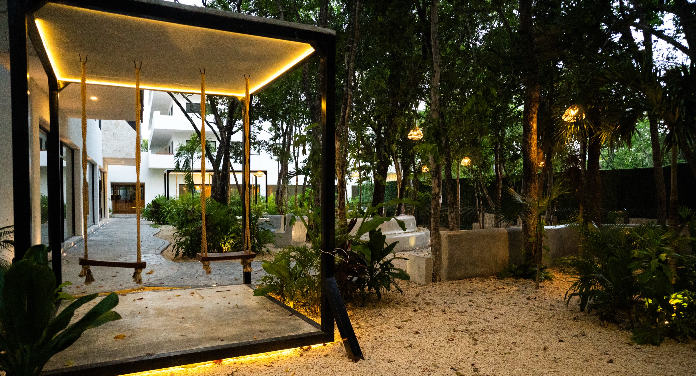 Lit glass pavilion and swing in the central courtyard at Town Center Zamá