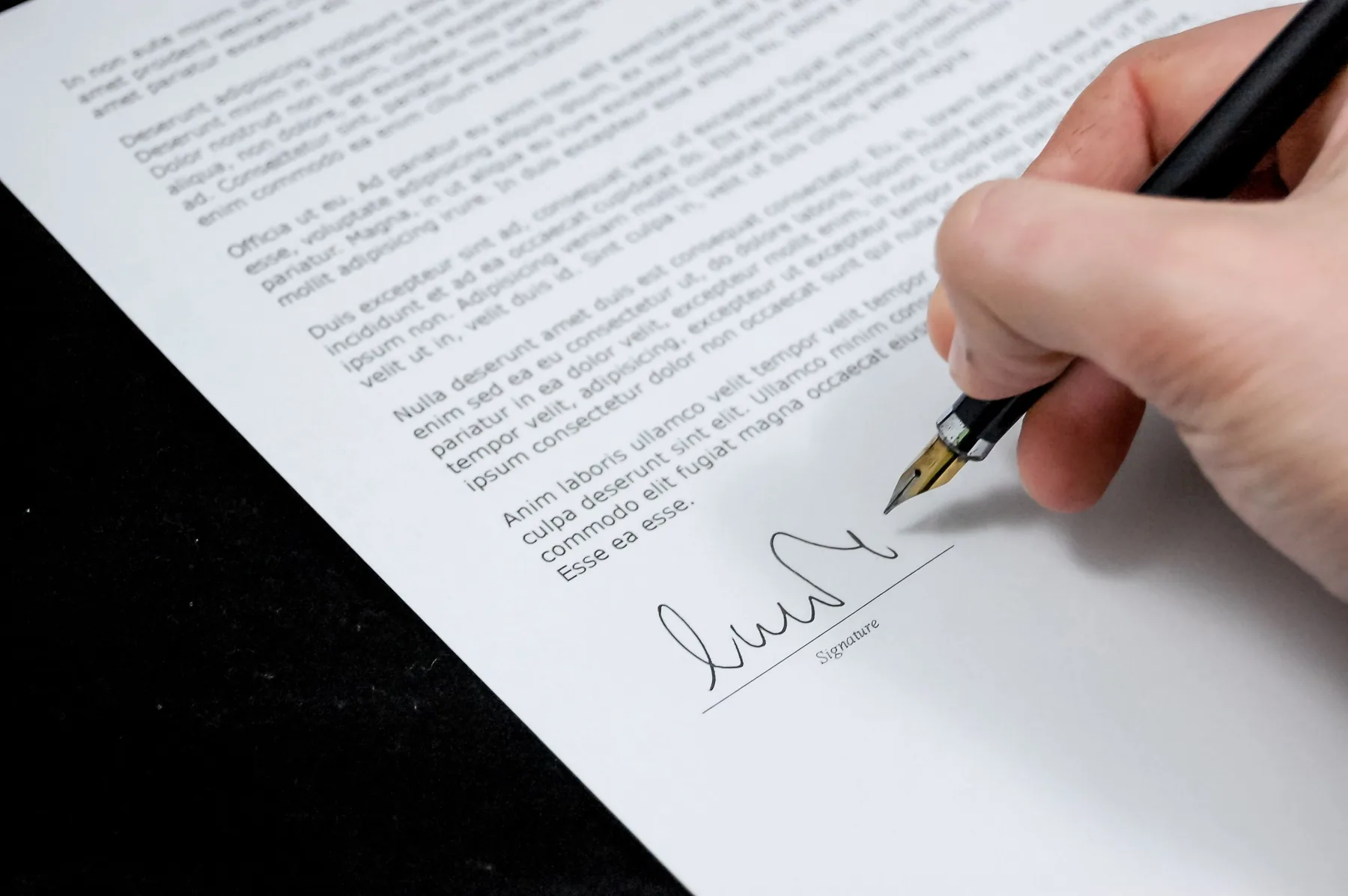 Hand signing a printed contract with a fountain pen on a dark desk