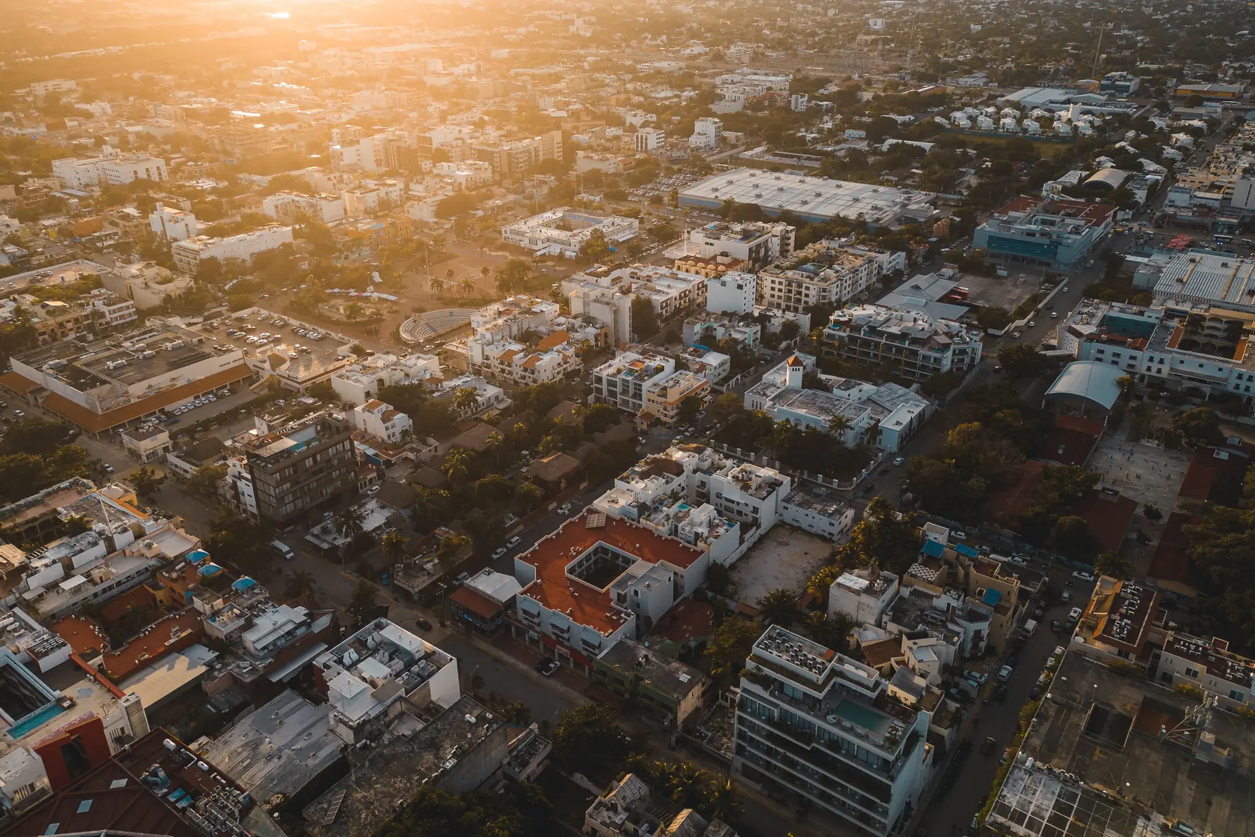 Aerial view of Playa del Carmen at sunset, dense blocks of low buildings with rooftops, pools and streets running back from the coast
