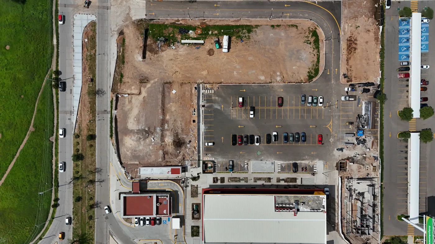 Top-down aerial view of a commercial lot: finished parking on one side, graded bare ground on the other